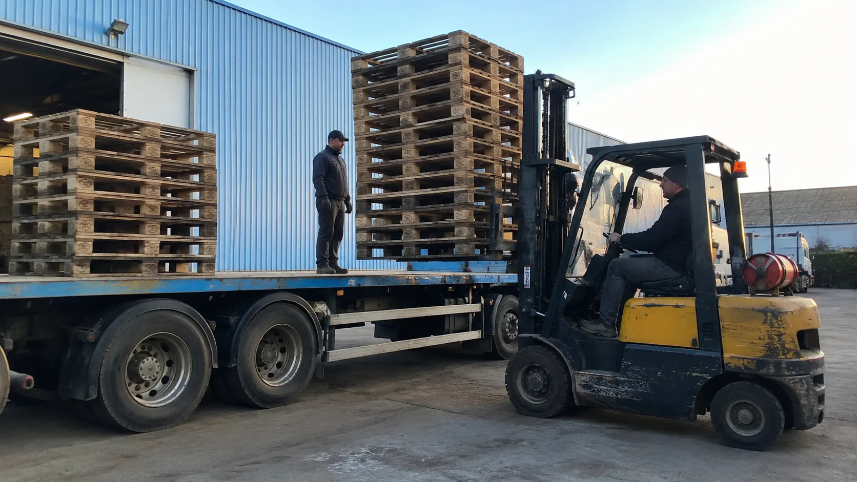 Heftruck tilt een stapel gebruikte pallets op een vrachtwagen op het buitenterrein